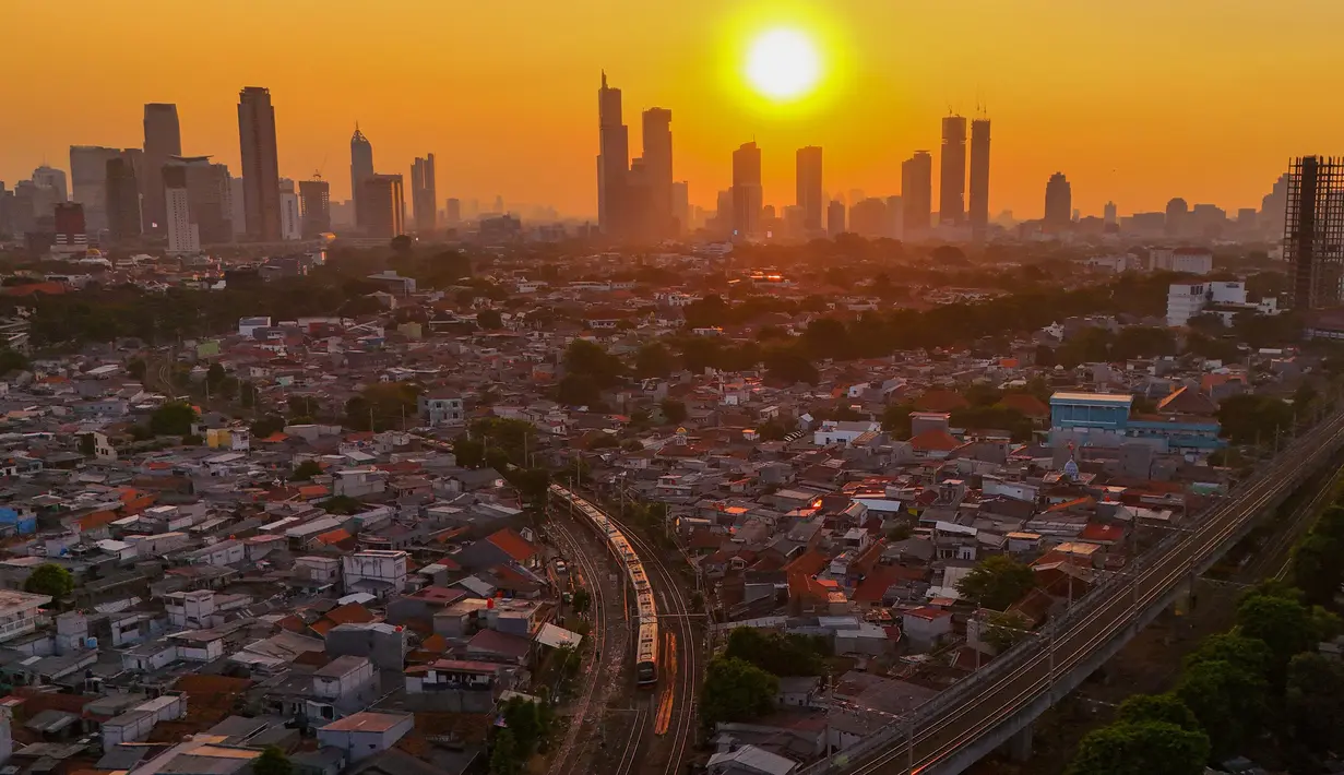 Rangkaian kereta melewati kawasan padat penduduk dengan latar belakang gedung bertingkat saat matahari terbenam di kawasan Manggarai, Jakarta, Kamis, 16/07/ 2026. (KLY/ Arie Basuki)