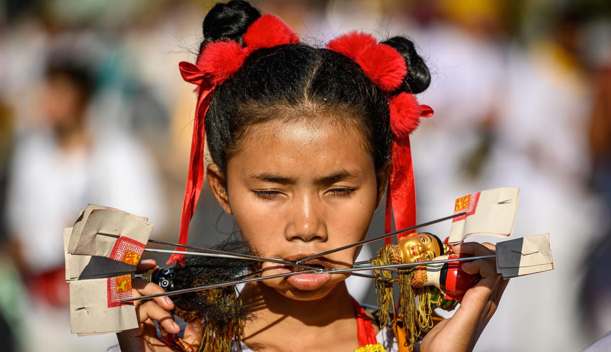 Seorang wanita menusuk pipinya dengan besi  saat mengikuti prosesi perayaan Festival Vegetarian tahunan di Phuket, Thailand, Kamis (3/10/2019). Festival dimulai pada malam pertama bulan lunar kesembilan dan berlangsung selama sembilan hari. (AFP Photo/Mladen Antonov)