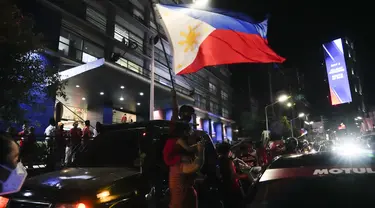 Seorang pendukung mengibarkan bendera saat mereka tiba di markas besar Ferdinand "Bongbong" Marcos Jr di Mandaluyong, Filipina pada Senin malam (9/5/2022). Ferdinand Marcos Jr., putra mendiang Ferdinand Marcos, diktator Filipina yang terguling, jauh memimpin dalam penghitungan suara tidak resmi pemilu presiden hari Senin. (AP Photo/Aaron Favila)