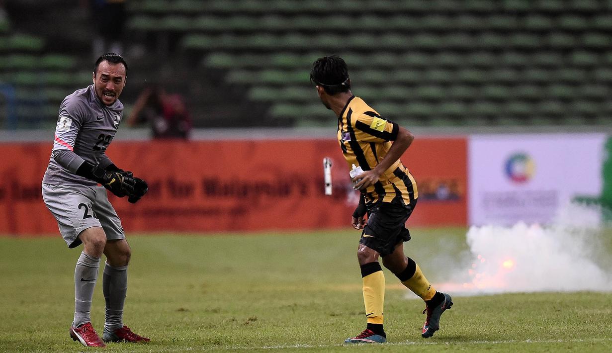 Pemain Malaysia, Nazirul Naim, dan kiper, Khairul Fahmi, berlari saat penonton melempar suar ke lapangan saat laga melawan Arab Saudi pada Pra Piala Dunia 2018 di Malaysia, Selasa (8/9/2015). (AFP Photo/Manan Vatsyayana)