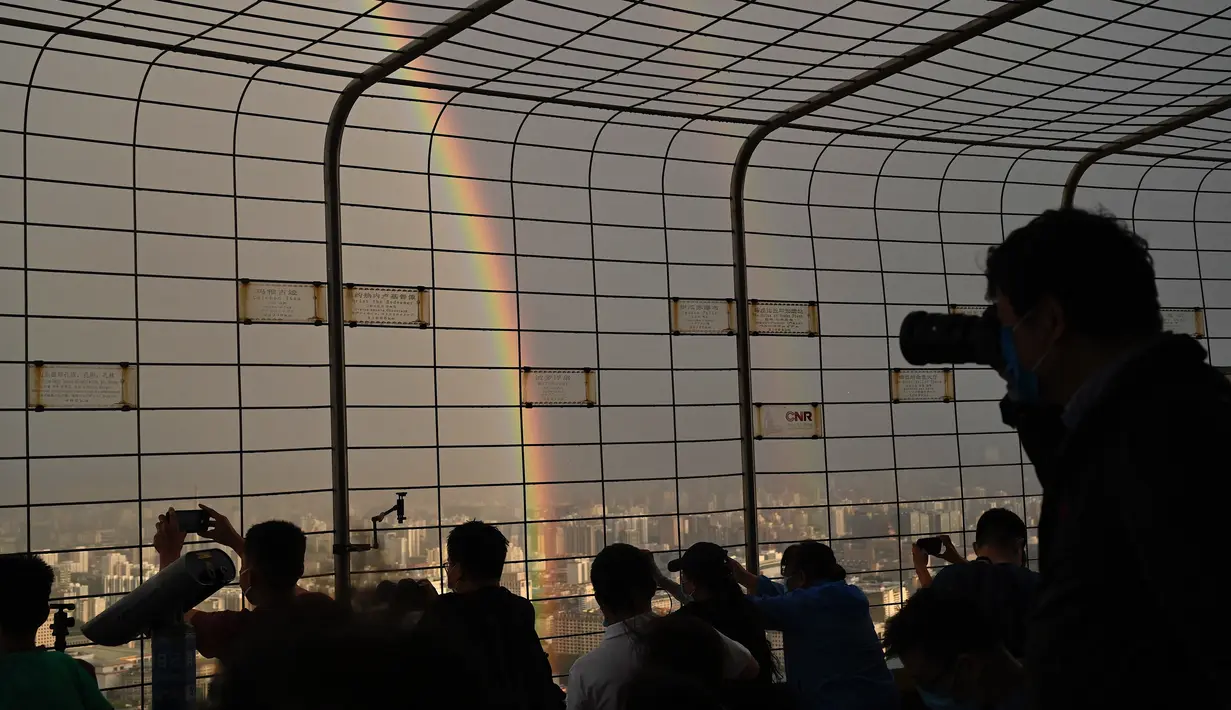 Orang-orang mengambil foto pelangi ganda melalui pagar di Central Television Tower di Beijing (26/8/2021). Keindahan pelangi ganda dimanfaatkan warga Beijing untuk diabadikan lewat foto dan berfoto dengan latar pelangi itu. (AFP/Jade Gao)