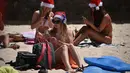 Turis memakai topi Santa foto di sebelah pohon Natal selama Hari Natal di Pantai Bondi di Sydney, Australia (25/12). (AFP Photo/Peter Parks)