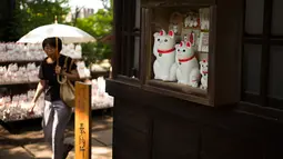Seorang wanita melewati patung-patung kucing yang disebut maneki-neko di kuil Gotokuji, Tokyo, Jepang, 6 Agustus 2018. Di tiap sudut kuil, patung kucing tersebut hadir dalam berbagai ukuran  dengan jumlah yang nyaris tak terhingga. (AFP/Martin BUREAU)