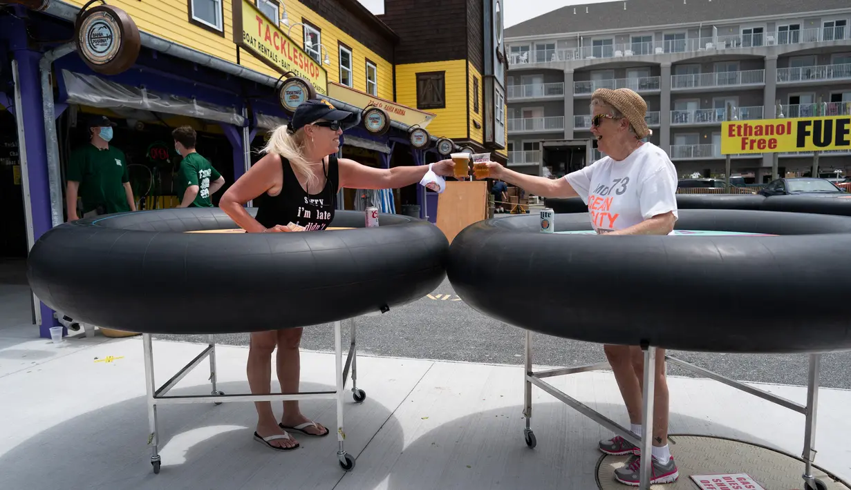 Para tamu mencoba meja portabel yang bentuknya menyerupai ban pelampung untuk menjaga jarak pelanggan di Fish Tales Bar & Grill di Ocean City, Maryland, Jumat (29/5/2020). Pengunjung akan berdiri di bagian tengah meja bundar itu yang dilengkapi roda untuk memudahkan pergerakan. (Alex Edelman/AFP)