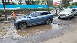 Pengendara kendaraan roda dua dan roda empat terpaksa harus memperlambat laju kendaraan untuk menghindari kerusakan jalan dan mencegah terjadinya kecelakaan lalu lintas. Tampak dalam foto, sejumlah pengendara melewati kerusakan di Jalan Mitra Bahari, Penjaringan Jakarta Utara, Selasa (3/2/2026). (merdeka.com/Arie Basuki)