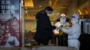 Seorang pekerja hotel dengan pakaian pelindung diri atau hazmat membantu seorang tamu membayar pembeliannya di Hotel Shangri-La pada Olimpiade Musim Dingin 2022, Rabu, 16 Februari 2022, di Beijing. (AP Photo/Jae C.Hong)