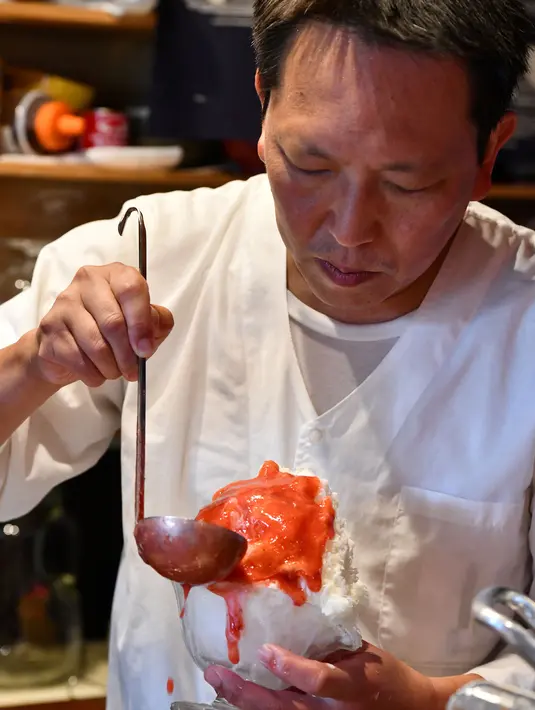 Pemilik toko Koji Morinishi menuangkan sirup ke es alami saat membuat kakigori di distrik Yanaka Tokyo, Jepang (21/6/2019). kakigori biasanya dihidangkan bersama aneka topping, potongan buah, es krim, hingga kacang merah. (AFP Photo/Toshifumi Kitamura)