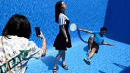Pengunjung berfoto di karya seni Swimming Pool dalam sebuah pameran pameran bertajuk "The Confines of the Great Void" di Museum CAFA, Beijing, 23 Juli 2019. Karya seni unik itu pun banyak dikunjungi wisatawan yang ingin punya foto underwater keren tanpa harus basah-basahan. (WANG Zhao/AFP)