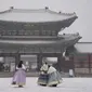 Pengunjung yang mengenakan masker untuk membantu mengekang penyebaran virus corona berfoto di tengah salju di Istana Gyeongbok, salah satu landmark terkenal Korea Selatan, di Seoul, Korea Selatan, Rabu (19/1/2022). (AP Photo/Lee Jin-man)