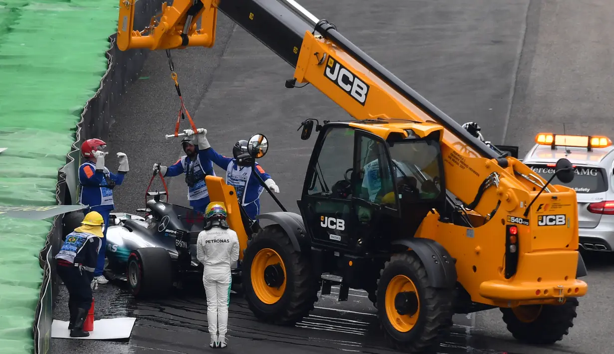 Petugas mengangkat mobil Lewis Hamilton usai menabrak dinding pembatas lintasan saat kualifikasi F1 GP Brasil di sirkuit Interlagos di Sao Paulo, Brasil (11/11). Hamilton gagal finis di kualifikasi GP Brasil. (AFP Photo/Nelson Almeida)