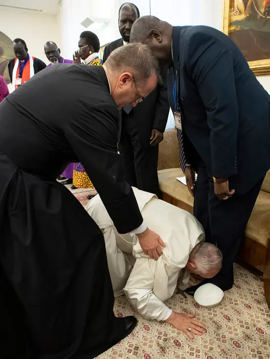 Paus Fransiskus berlutut dan mencium kaki para pemimpin Sudan Selatan dalam pertemuan di tengah retret spiritual di Vatikan, Kamis (11/4). Para pemimpin itu terpana ketika paus, yang menderita sakit kaki kronis, dibantu oleh asistennya berlutut dengan susah payah. (Vatican Media/Handout via REUTERS)