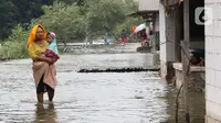 Seorang ibu menggendong anaknya sambil menerobos banjir rob yang menggenangi rumah dan tambak warga di Desa Pantai Mekar, Muaragembong, Bekasi, Senin (6/12/2021). Banjir rob telah menggenangi wilayah tersebut selama empat hari akibat kenaikan permukaan air laut. (Liputan6.com/Herman Zakharia)