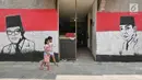 Dua anak melintasi sisi tembok warga yang dindingnya dihiasi lukisan mural Presiden pertama RI, Sukarno di Kampung Pejaten, Jakarta, Senin (30/4). Mural motif warna-warni itu digagas warga untuk memperindah kampung mereka. (Liputan6.com/Herman Zakharia)