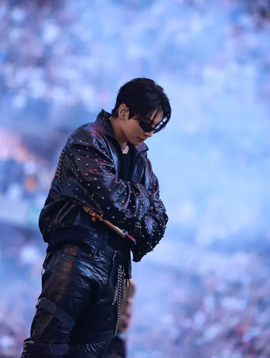 Jung Kook kenakan busana serba kulit hitam. Memadukan celana panjang dengan banyak ikat pinggang, sarung tangan motor bergesper, dan jaket berkerah tinggi yang dihiasi kancing logam Le City [Balenciaga]