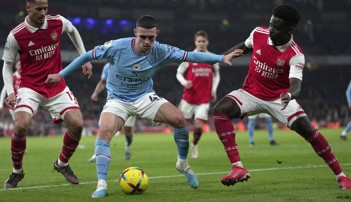 Pemain Manchester City, Phil Foden (tengah) berusaha melewati pemain Arsenal, Bukayo Saka (kanan) dan William Saliba pada laga pekan ke-23 Liga Inggris 2022/2023 yang berlangsung di Emirates Stadium, London, Kamis (16/02/2023) WIB. (AP Photo/Kin Cheung)
