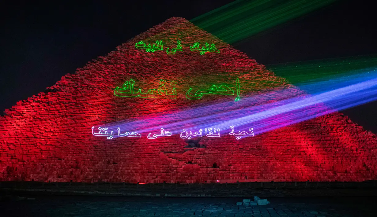 Kementerian barang antik Mesir menerangi Piramida Besar Mesir dengan pesan dukungan bagi tenaga kesehatan yang memerangi pandemi corona Covid-19 di Giza, Senin (30/3/2020). Piramida tersebut menampilkan pesan dalam bahasa Arab dan Inggris dalam cahaya berwana biru dan hijau. (AP/Nariman El-Mofty)