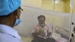 Petugas medis melihat seorang pasien minum air kelapa saat dia duduk di bawah kelambu di bangsal demam berdarah sebuah rumah sakit pemerintah di Allahabad, India (30/8/2021). (AFP/Sanjay Kanojia)