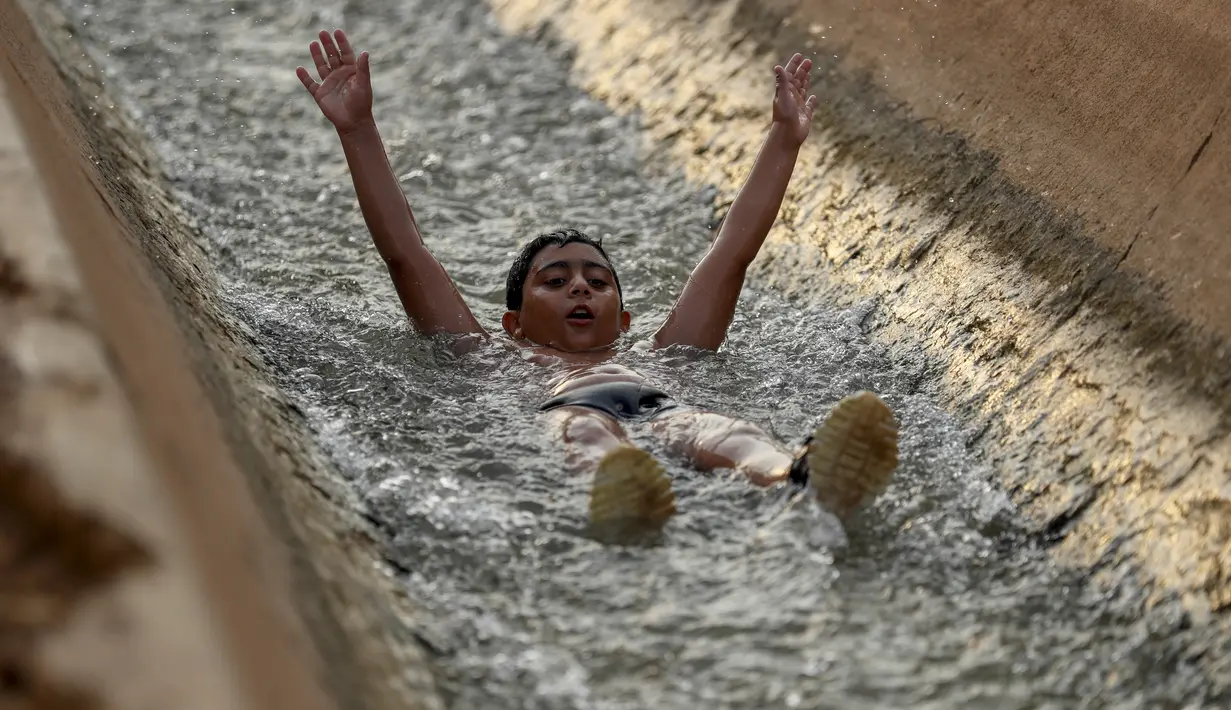 Seorang anak bermain di aliran mata air yang digunakan untuk irigasi untuk mendinginkan tubuh saat suhu udara mencapai 44 derajat Celcius di kota Jericho, Tepi Barat (1/9/2020). (AFP Photo/Ahmad Gharabli)