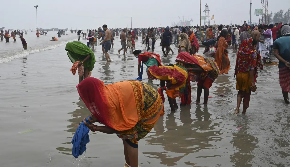 Peziarah Hindu mencuci pakaian setelah berenang selama festival Makar Sankranti di pertemuan Sungai Gangga dan Teluk Benggala di Pulau Sagar, selatan Kolkata (14/1/2022). India tengah menghadapi lonjakan kasus COVID-19 yang dipicu oleh varian Omicron yang sangat menular. (AFP/Dibyangshu Sarkar)