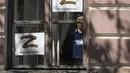 Seorang wanita melihat melalui jendela dengan seprai bergambar huruf Z yang telah menjadi simbol militer Rusia dan tagar bertuliskan 'Kami tidak meninggalkan milik kami' selama perayaan menandai ulang tahun ke 318 kota Kronstadt, di luar St. Petersburg, Rusia (21/5/2022). (AP Photo/Dmitri Lovetsky)
