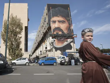 Warga setempat berjalan di depan mural legenda sepak bola, Diego Armando Maradona di San Giovanni a Teduccio, Italia (28/2). Mural tersebut digambar di sebuah bangunan pemukiman warga di distrik yang dikenal dengan Bronx. (AFP/Renato Esposito)