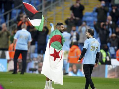 Gelandang Manchester City, Riyad Mahrez mengibarkan bendera Palestina saat merayakan timnya meraih gelar Liga Inggris usai mengalahkan Everton di stadion Etihad di Manchester, Minggu (23/5/2021). City menang besar atas Everton dengan skor 5-0. (AP Photo / Dave Thompson, Pool)