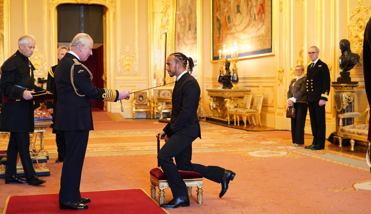 Pembalap Lewis Hamilton, menerima gelar kebangsawanan dari Pangeran Charles untuk prestasinya di bidang olahraga, di Kastil Windsor, Rabu (15/12/2021). Pemegang gelar juara dunia balapan Formula Satu tujuh kali ini diberi gelar Knight Bachelor. (Dominic Lipinski/PA via AP)
