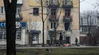 Seorang pria berjalan melewati sebuah gedung apartemen pada 2 Maret yang dirusak oleh penembakan Rusia di Mariupol, Ukraina. (Evgeniy Maloletka/AP)