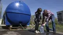 <p>Seorang gadis Lisa membantu seorang pria mengisi kaleng dengan air dari tangki air yang dipasang untuk penduduk Toretsk, di Ukraina timur, pada 25 April 2022. Penduduk Toretsk tidak memiliki akses air selama lebih dari dua bulan karena perang Rusia Ukraina. (AP Photo/Evgeniy Maloletka)</p>