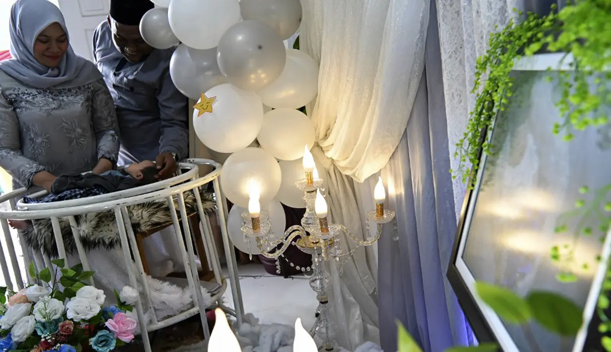 Sepasang suami istri menghibur bayi mereka yang baru lahir saat prosesi aqiqah di Banda Aceh, Aceh, 4 November 2021. Aqiqah adalah tradisi menyambut bayi yang baru lahir dalam agama Islam. (CHAIDEER MAHYUDDIN/AFP)