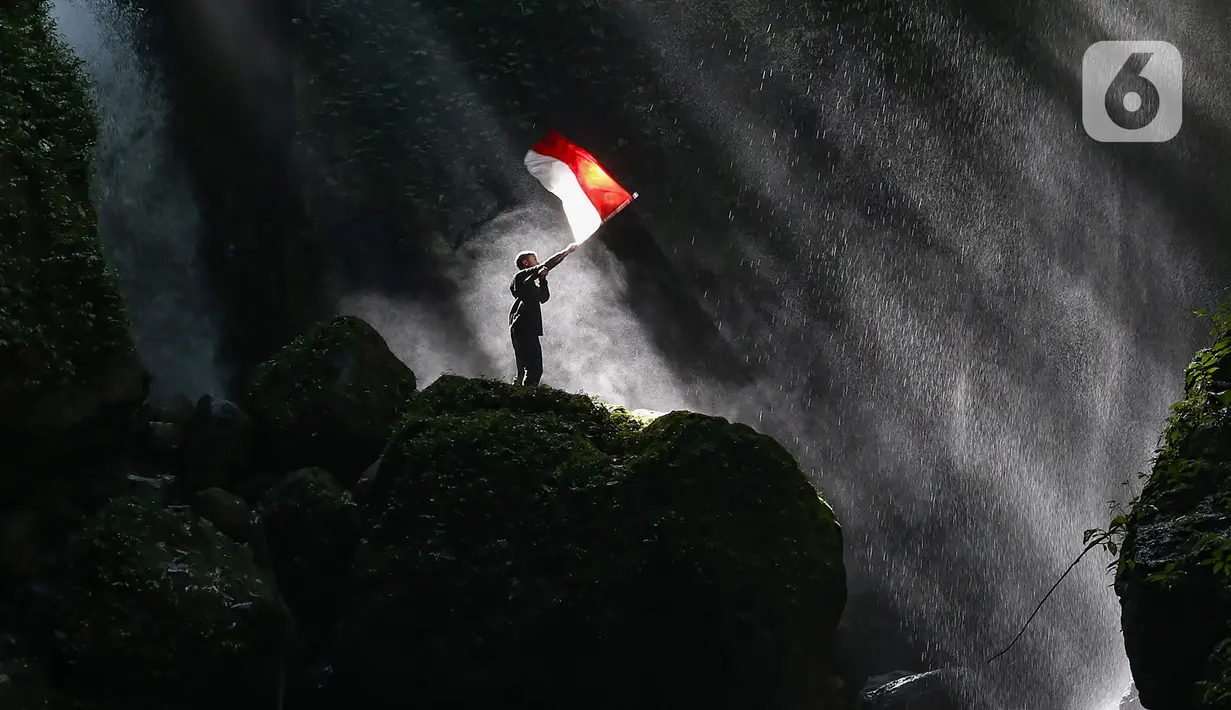 Pengunjung berdiri di atas batu besar sambil memegang bendera Merah Putih di Curug Walet, Pamijahan, Bogor, Jawa Barat, Minggu (24/12/2023). Curug yang terkenal dengan keindahannya ini berada di Desa Ciasihan, Kecamatan Pamijahan. (merdeka.com/Arie Basuki)