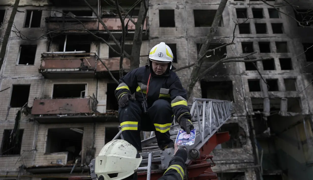 Petugas pemadam kebakaran Ukraina memegang sebuah foto, ditemukan di puing-puing, saat mereka bekerja di sebuah bangunan penduduk setelah terkena tembakan artileri Rusia di Kiev, Senin, 14 Maret 2022. (AP Photo/Vadim Ghirda)