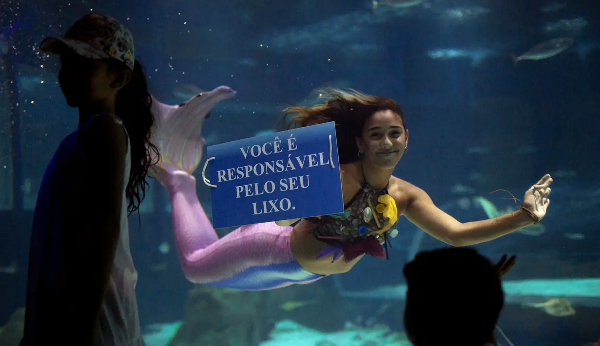 Mahasiswi biologi laut Brasil Isabela Cardoso (21) tersenyum dengan pengunjung saat berenang seperti putri duyung memprotes bahaya pencemaran laut dalam kehidupan laut di Rio de Janeiro di AquaRio, Brasil (14/1). (AFP Photo/Mauro Pimentel)