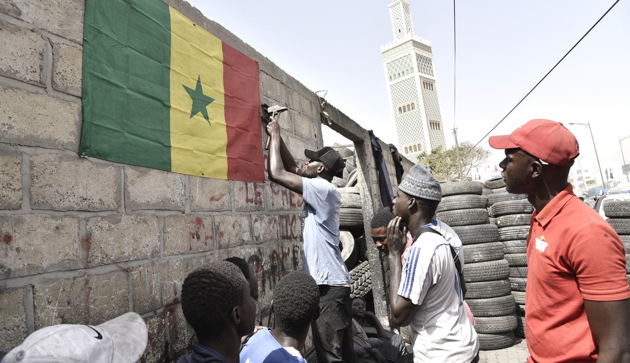 Pendukung menggantung bendera nasional Senegal di luar bengkel ban di Dakar (4/2/2022). Senegal akan bertanding melawan Mesir pada babak final Piala Afrika 2021 di Paul Biya stadium, Senin (7/2/2022) dini hari WIB besok. (AFP/Seyllou)
