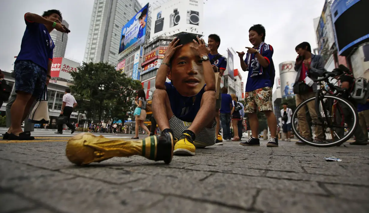 Suporter Timnas Jepang menggunakan topeng bergambar Yuto Nagatomo terduduk usai menyaksikan kekalahan Samurai Biru lewat layar lebar di Shibuya, Tokyo, (25/6/2014). (REUTERS/Issei Kato)