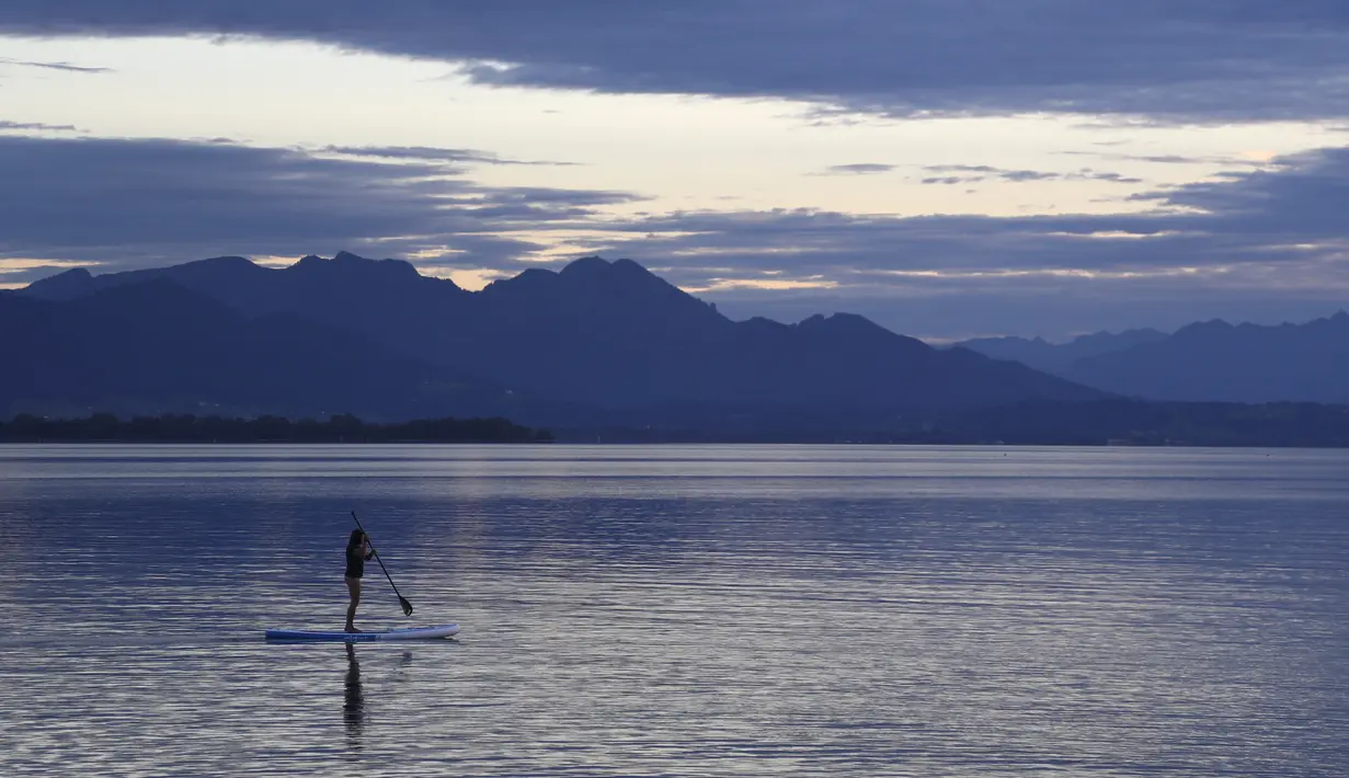Seorang wanita muda mengontrol papan dayung, di danau Chiemsee saat matahari terbenam di Chieming, Jerman, Selasa, (25/8/2020). (AP Photo / Matthias Schrader)