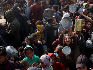 Warga, termasuk anak-anak pengungsi Palestina berkumpul untuk menerima bantuan makanan yang didistribusikan di Deir al-Balah, Jalur Gaza tengah pada 16 Januari 2025. (Eyad BABA/AFP)