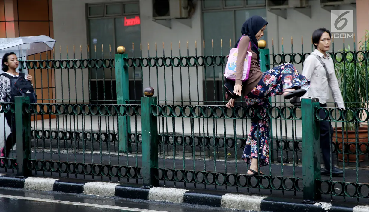 Seorang wanita melompati pagar pembatas di Stasiun Cikini, Jakarta, Rabu, (20/12). Banyaknya penumpang yang mencari jalan pintas dengan melompat pagar untuk menuju akses pintu keluar menyebabkan kemacetan di kawasan stasiun. (Liputan6.com/Johan Tallo)