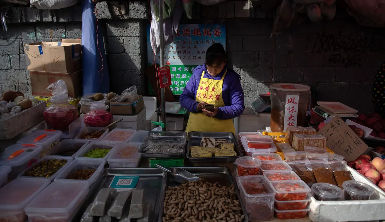 Seorang pedagang melihat ponsel miliknya di pasar di Beijing (20/11). (AFP Photo/Nicolas Asfouri)