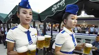 Dua orang pelayan yang mengenakan seragam menyajikan bir selama festival di Korea Utara. Bir Taedonggang pada umumnya terkenal sebagai minuman kelas dunia. Minuman ini adalah bir hasil produksi negara dan dijadikan sebagai produk kebanggaan (AP)
