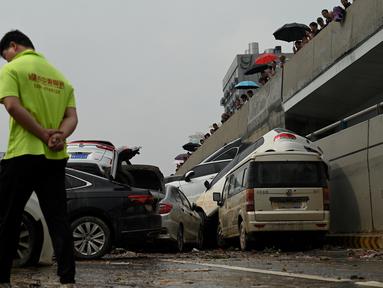 Orang-orang melihat mobil-mobil yang terendam banjir setelah hujan lebat melanda Zhengzhou di provinsi Henan, Kamis (22/7/2021). Henan, provinsi terbesar ketiga di China, yang merupakan rumah bagi sekitar 94 juta orang, telah dilanda badai hujan yang tidak biasa sejak akhir pekan. (Noel Celis/AFP)