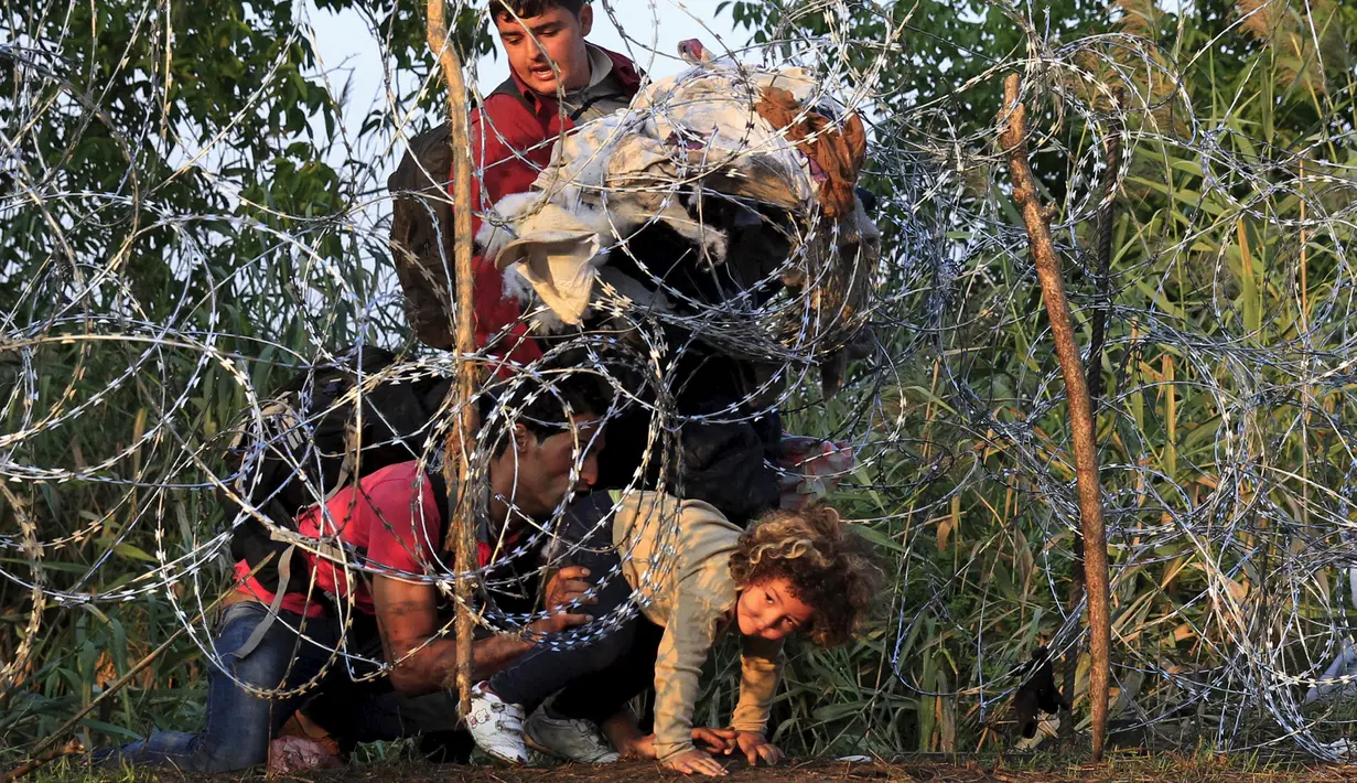 Seorang anak dibantu imigran Suriah berusaha melewati pagar berduri di wilayah Hungaria dekat perbatasan Serbia, wilayah Roszke, Kamis (27/8/2015). Hungaria berencana memperketat perbatasan bagian selatannya dari para pengungsi. (REUTERS/Bernadett Szabo)
