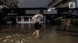 Warga mengunakan payung melintasi banjir di Jalan Kemang Raya, Jakarta Selatan, Selasa (4/10/2022). Hujan yang mengguyur wilayah Ibu Kota Jakarta mengakibatkan banjir menggenangi kawasan Kemang, Jakarta. (Liputan6.com/Johan Tallo)