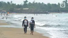Wisatawan yang mengenakan masker menikmati suasana Pantai Anyer di Cilegon, Banten, Minggu (25/10/2020). Akhir pekan dimanfaatkan warga Jakarta dan sekitarnya untuk berwisata dengan tetap menerapkan protokol kesehatan Covid-19. (merdeka.com/Arie Basuki)