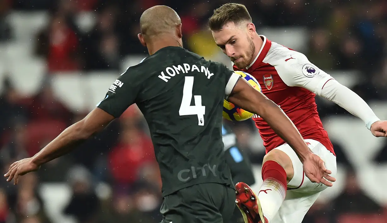 Bek Manchester City, Vincent Kompany berebut bola dengan gelandang Arsenal, Aaron Ramsey pada laga pekan ke-28 Premier League di Emirates Stadium,  Jumat (2/3). Manchester City mempermalukan Arsenal dengan skor telak 3-0. (Glyn KIRK/AFP)