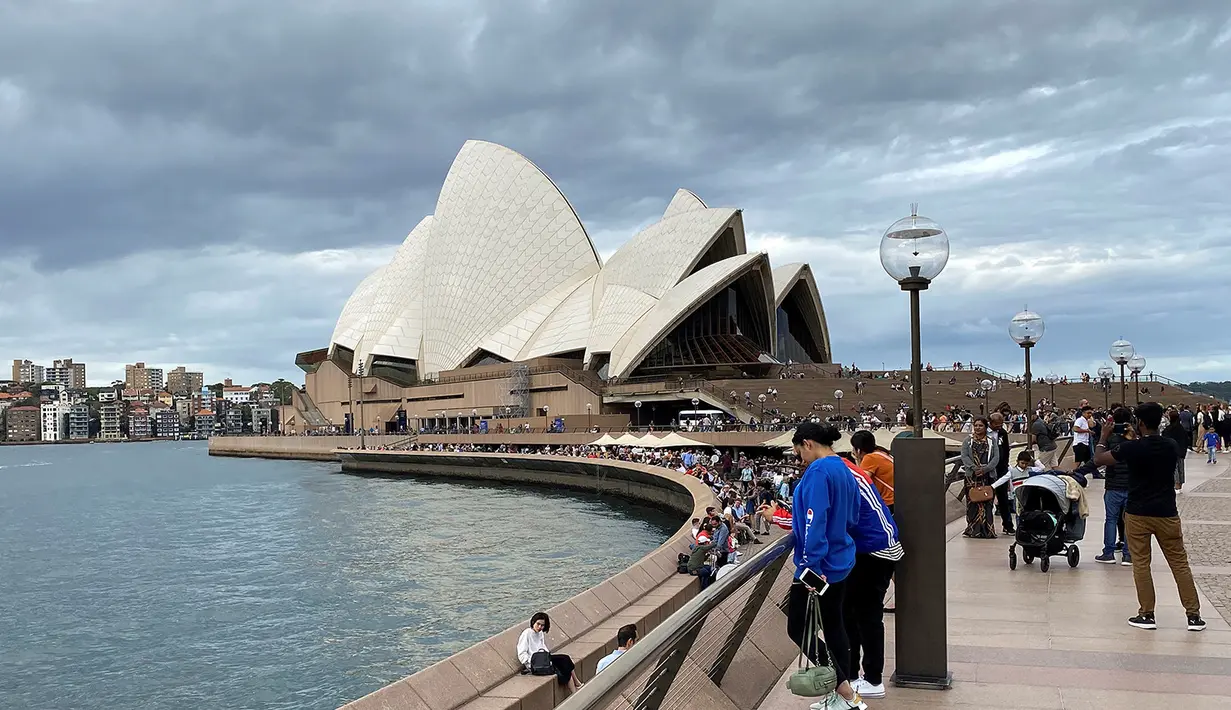 Warga berjalan di sepanjang Sydney Harbour dengan latar belakang pemandangan Sydney Opera House di Sydney pada 30 Desember 2017 (atas) dan pada 8 Maret 2020. (Saeed KHAN/AFP)