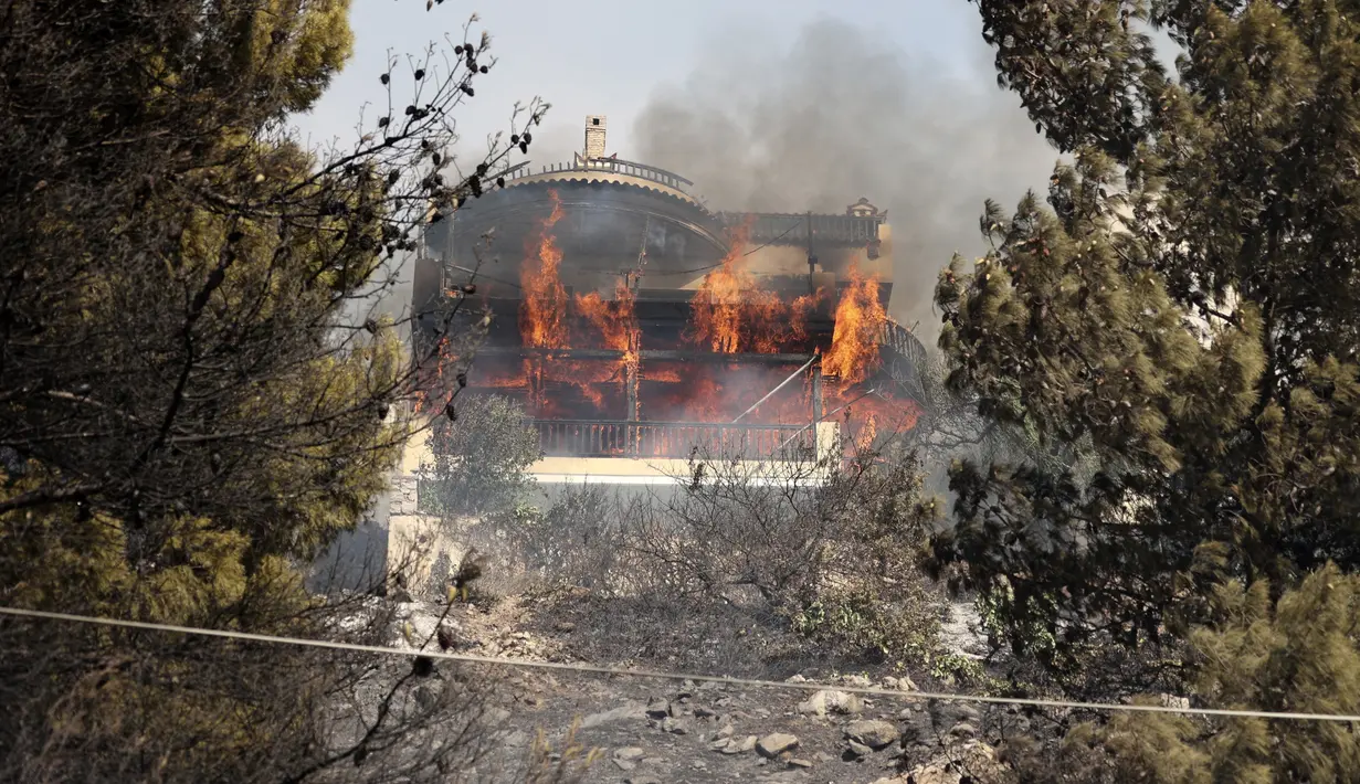 Api membakar sebuah rumah saat kebakaran hutan di pinggiran Voula, di selatan Athena, Yunani, Sabtu, 4 Juni 2022. Kebakaran hutan berkobar di luar kendali di pinggiran Athena, hingga merusak rumah-rumah dan mobil di permukiman warga. (AP Photo/Yorgos Karahalis)