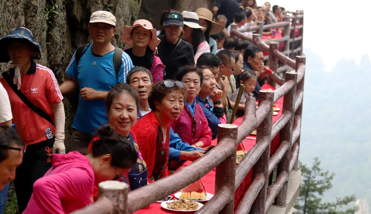 Wisatawan menyantap makanan pada acara perjamuan di sepanjang tepi tebing di Laojun Mountain provinsi Henan, China. Wisatawan menikmati berbagai suguhan makanan di jalanan selebar enam kaki yang menempel pada tebing setinggi 2.000 meter. (AFP)