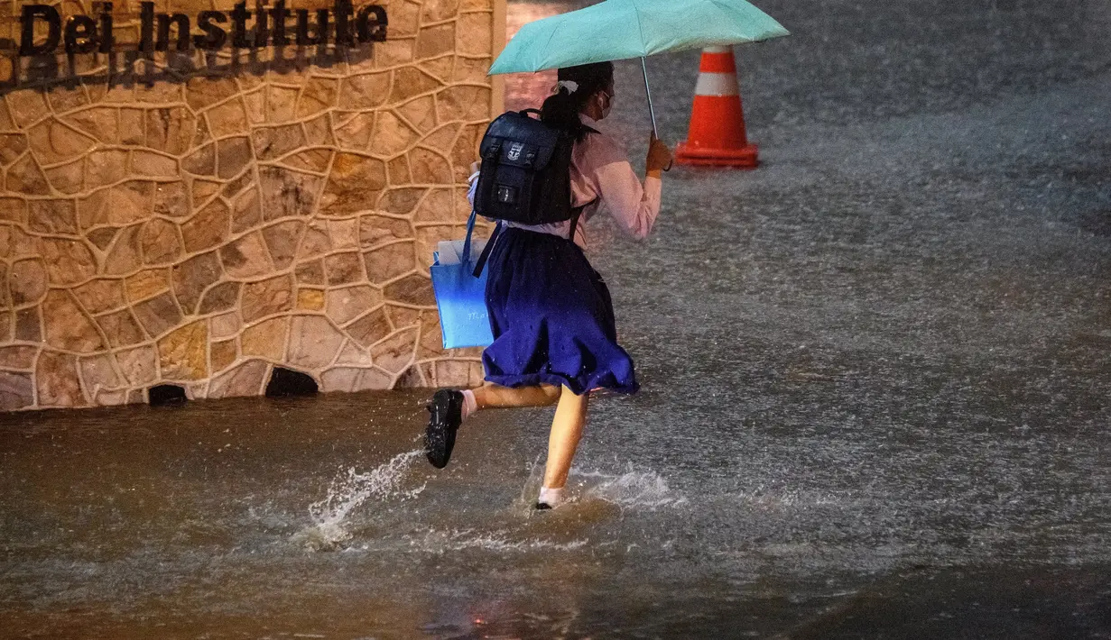 Seorang gadis sekolah berlari di jalan yang sebagian tergenang air saat hujan deras di Bangkok (23/9/2020). (AFP/Mladen Antonov)