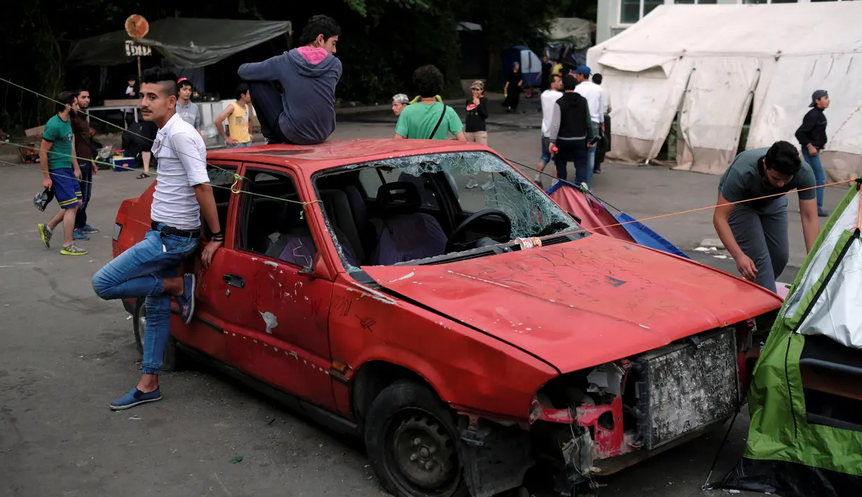Sejumlah imigran berdiri didekat mobil yang rusak di sebuah stasiun kereta api di sebuah kamp darurat bagi para migran dan pengungsi di perbatasan Yunani-Macedonia dekat desa Idomeni, Yunani, 10 Mei 2016. (REUTERS / Marko Djurica)